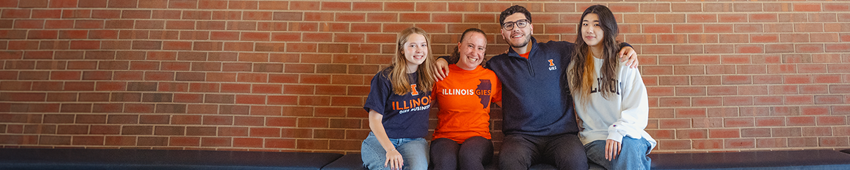 Four Gies students sitting together on a bench in front of a brick wall